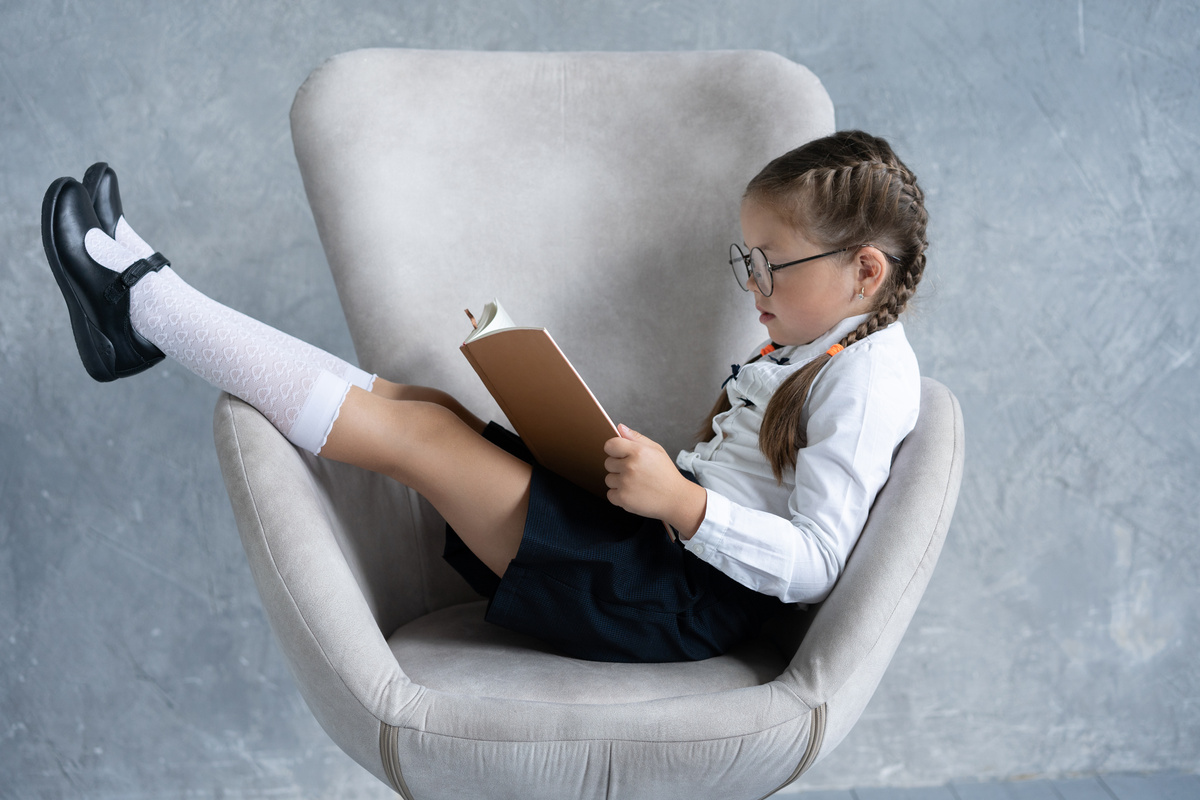 School girl focused on reading book sit in armchair.